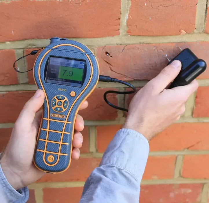 Moisture meter held against a brick wall during a water inspection