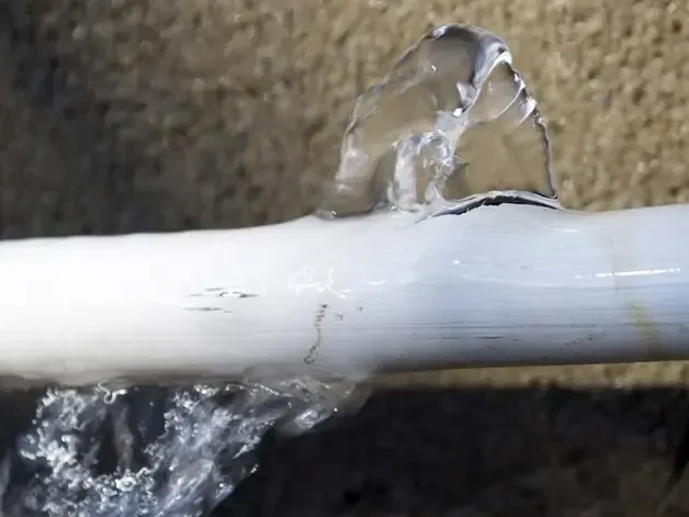 Water spraying through a split in a white supply pipe